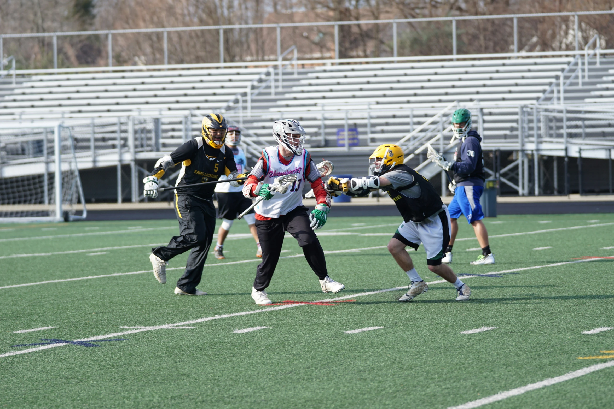 lacrosse teams running on a field with an athletic stadium behind