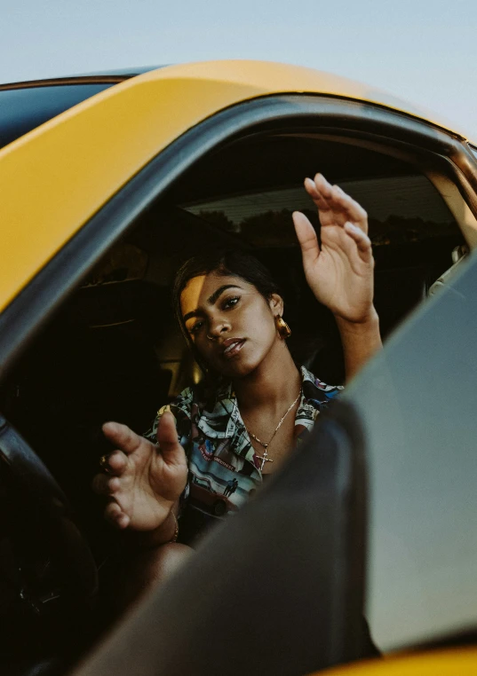 a person sitting in a yellow car with a hand up