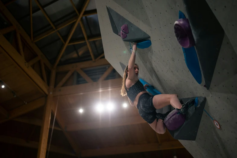 a female athlete climbing a wall with a green pad and purple vest on