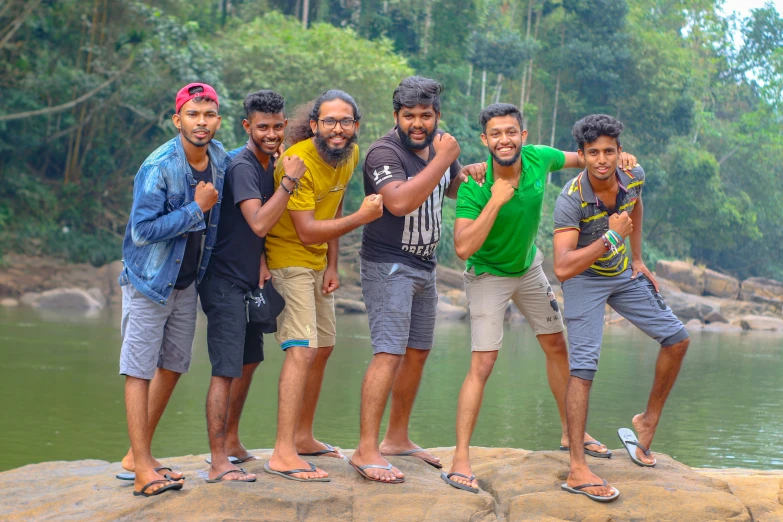 five smiling men pose on a rock in front of the water