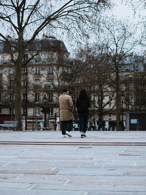 two people are walking down the street with trees