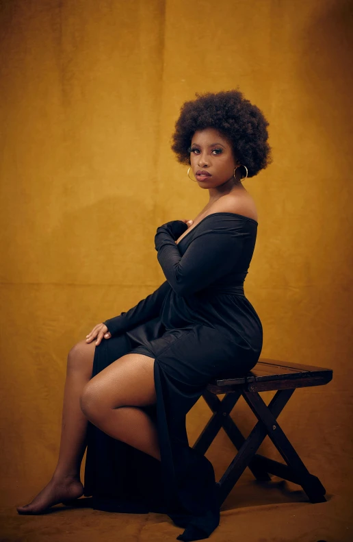 a woman in black sits on a stool in a brown backdrop