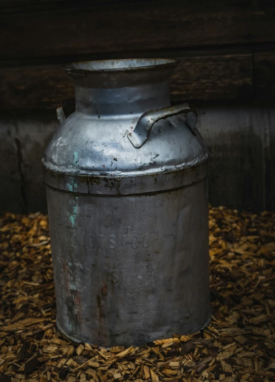 an old metal milk can is sitting on some dried wood