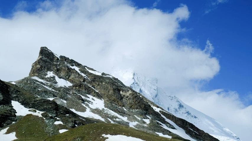 the mountain side of a snow capped area covered in green grass and shrubs