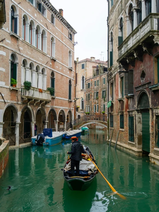 a man in a black jacket is rowing down a canal with several boats