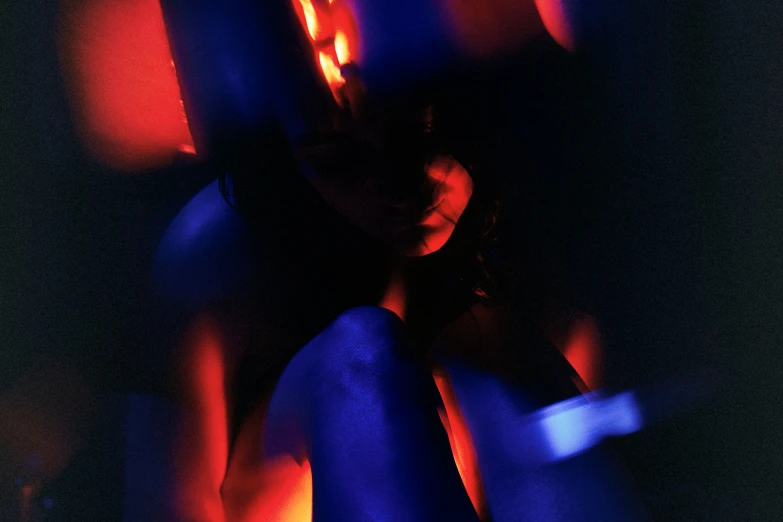 a girl sitting on her stomach in front of an orange and blue light