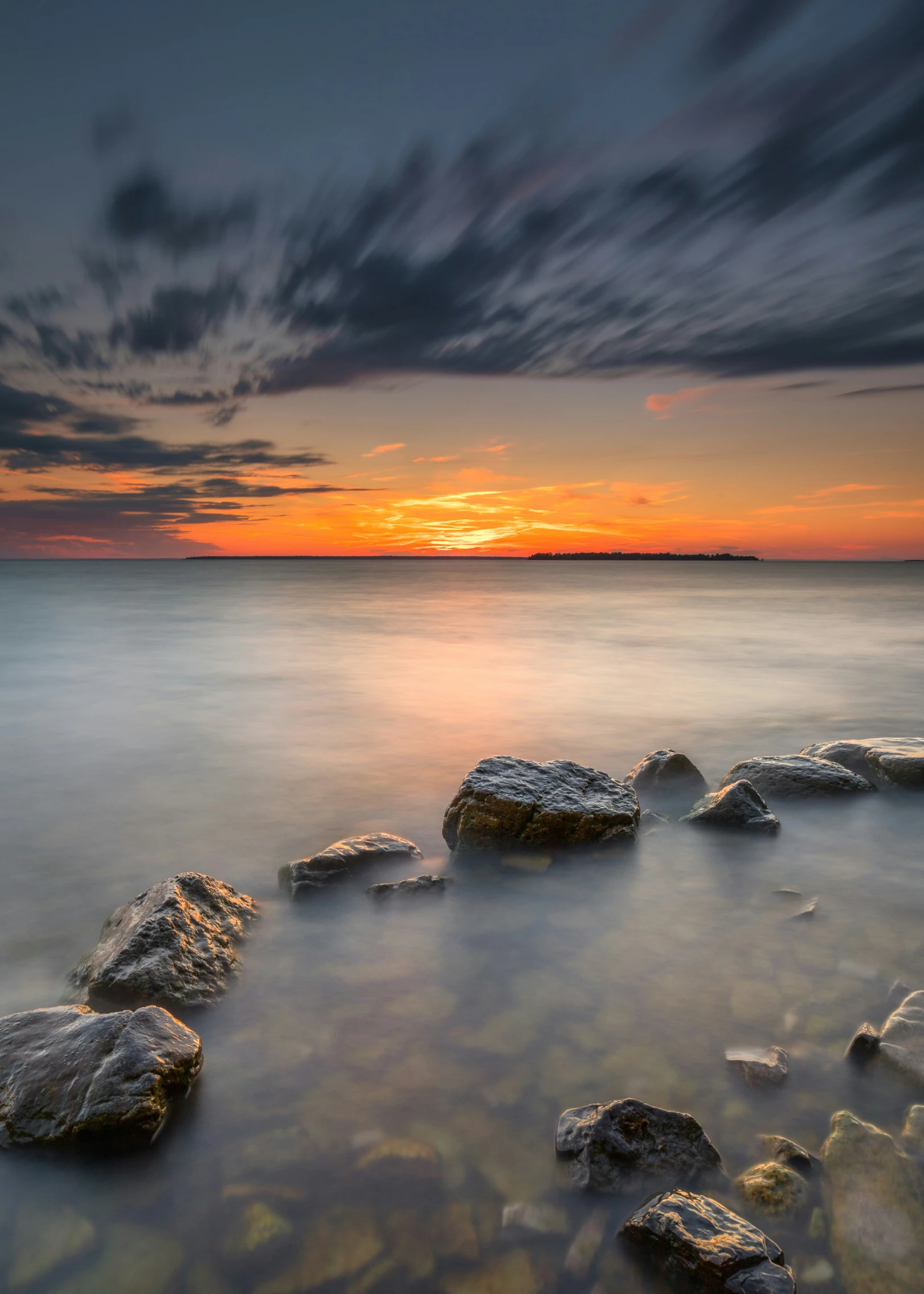 a sunrise at the beach with rocks in the foreground