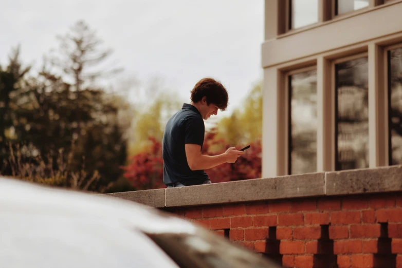 man texting on his cell phone while standing on the edge of a wall