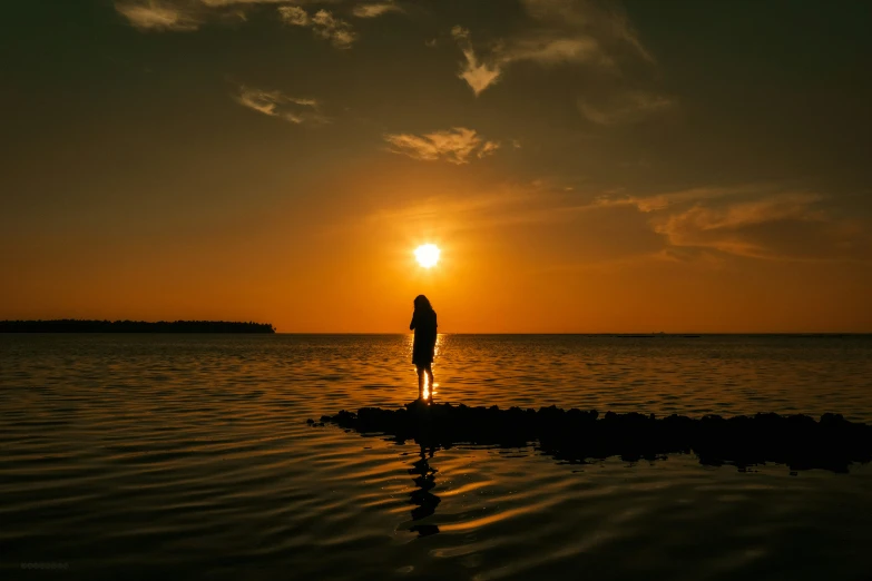 a person standing in the water looking at a sun setting