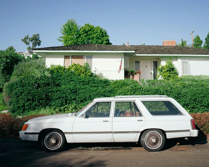 a white car is parked near bushes in front of a house