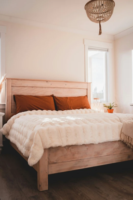 a bedroom with wood floors, a white bed with brown pillows and a chandelier hanging