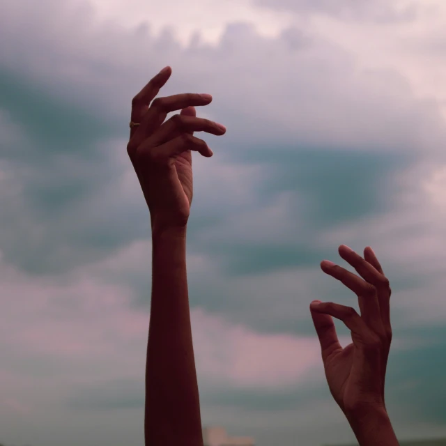 two hands reaching up toward the sky with the background