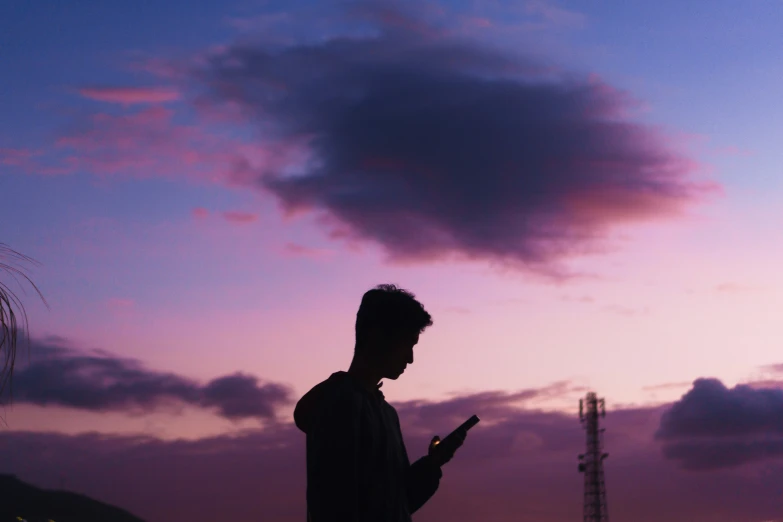 man holding his cell phone during the sunset with a cloud in the sky