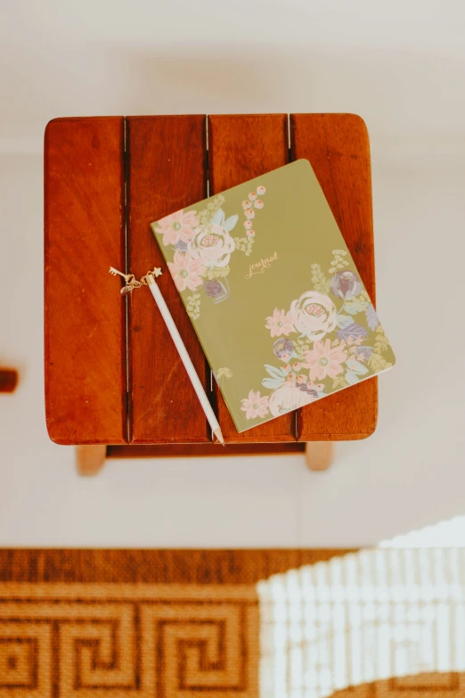 notebook and wooden stand displayed on table with floral pattern