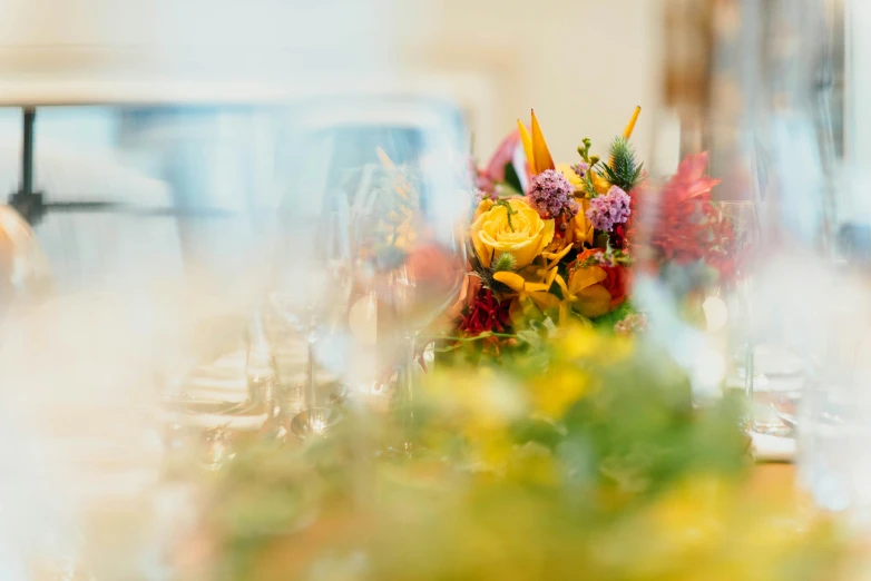 the blurry pograph has flowers in a vase and plates with glasses on it