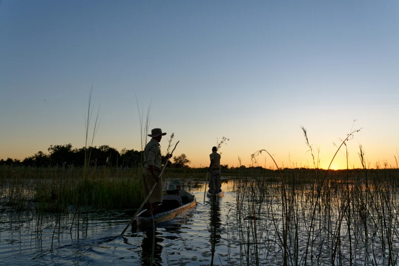 two men stand in a small boat in a marsh at sunset