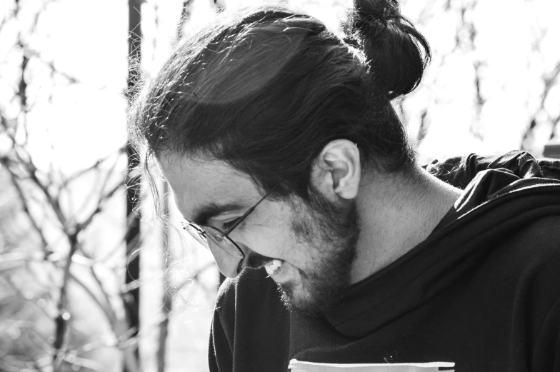 man with ponytail standing in woods looking at cell phone