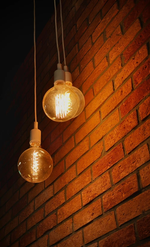 two glowing light bulbs hanging from a brick wall