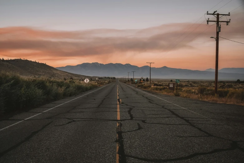 an empty road that looks out at mountains and clouds