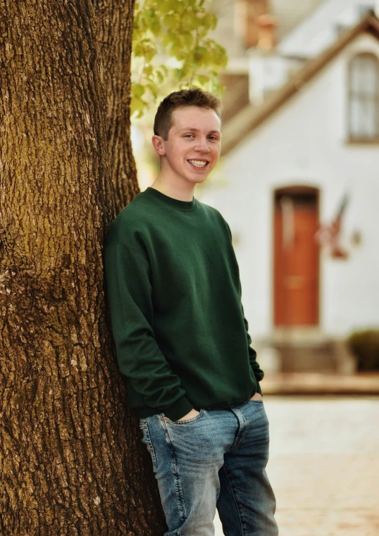 a young man is leaning against a tree