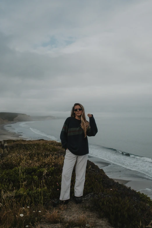 a woman in black sweater and white pants with surf in background