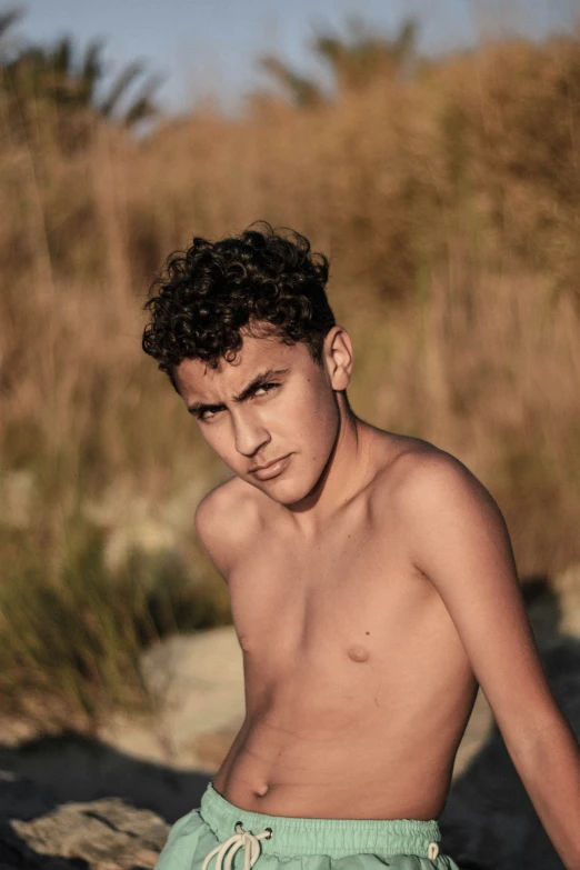 a young man wearing swim trunks sits on the beach