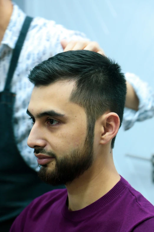 a man in an apron putting his hair styled with scissors