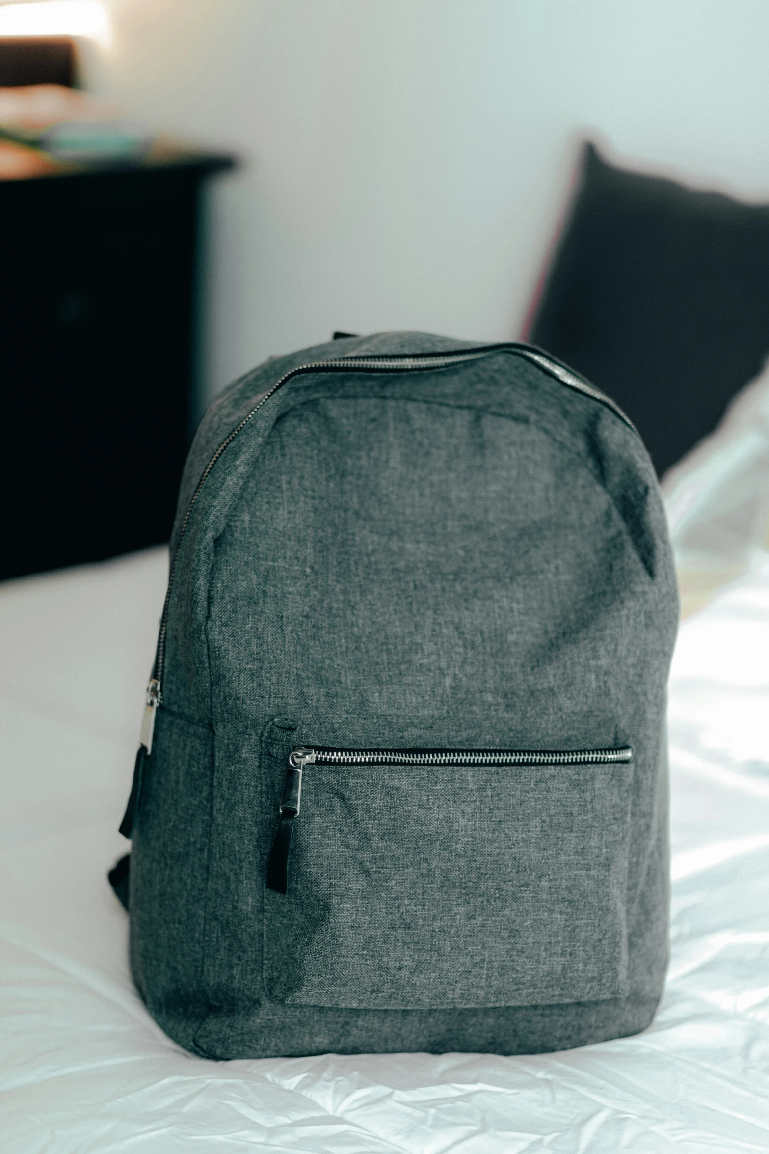 a dark grey backpack is placed on a bed