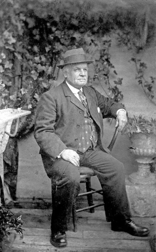 old pograph of man in suit and tie, sitting on chair