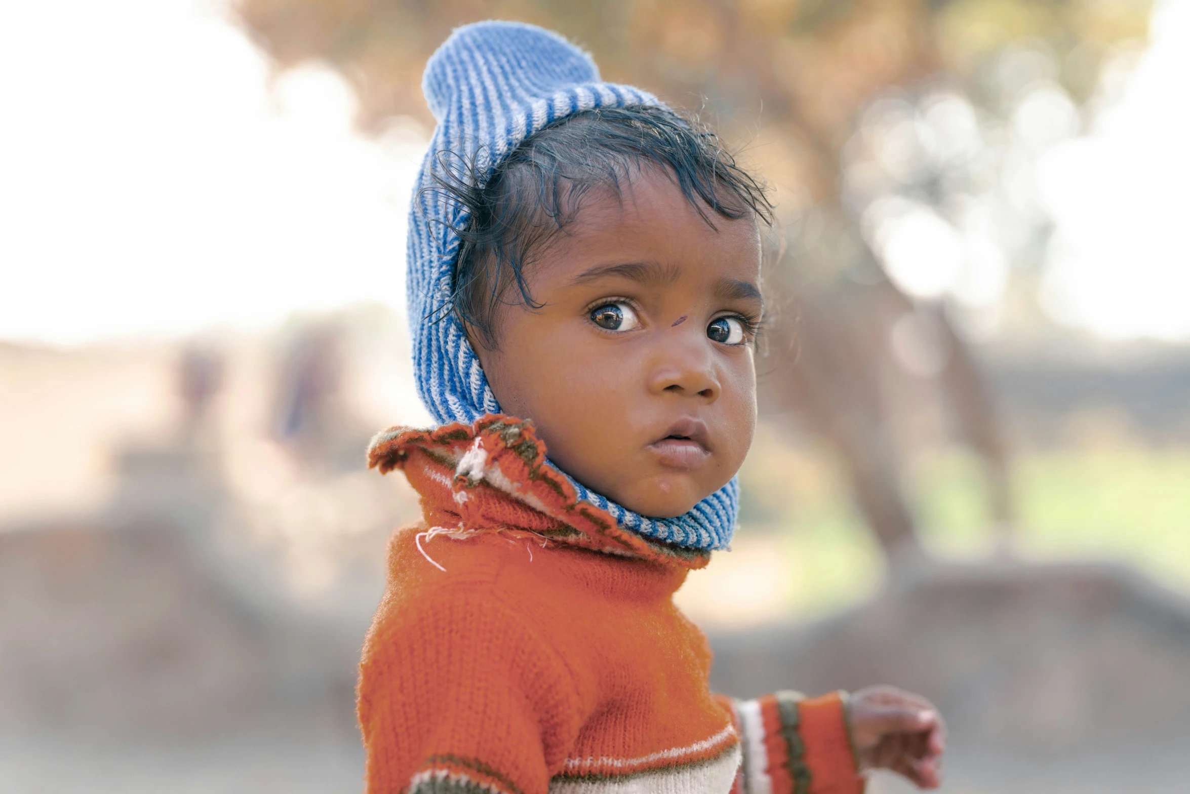 a small child with an orange sweater and blue hat