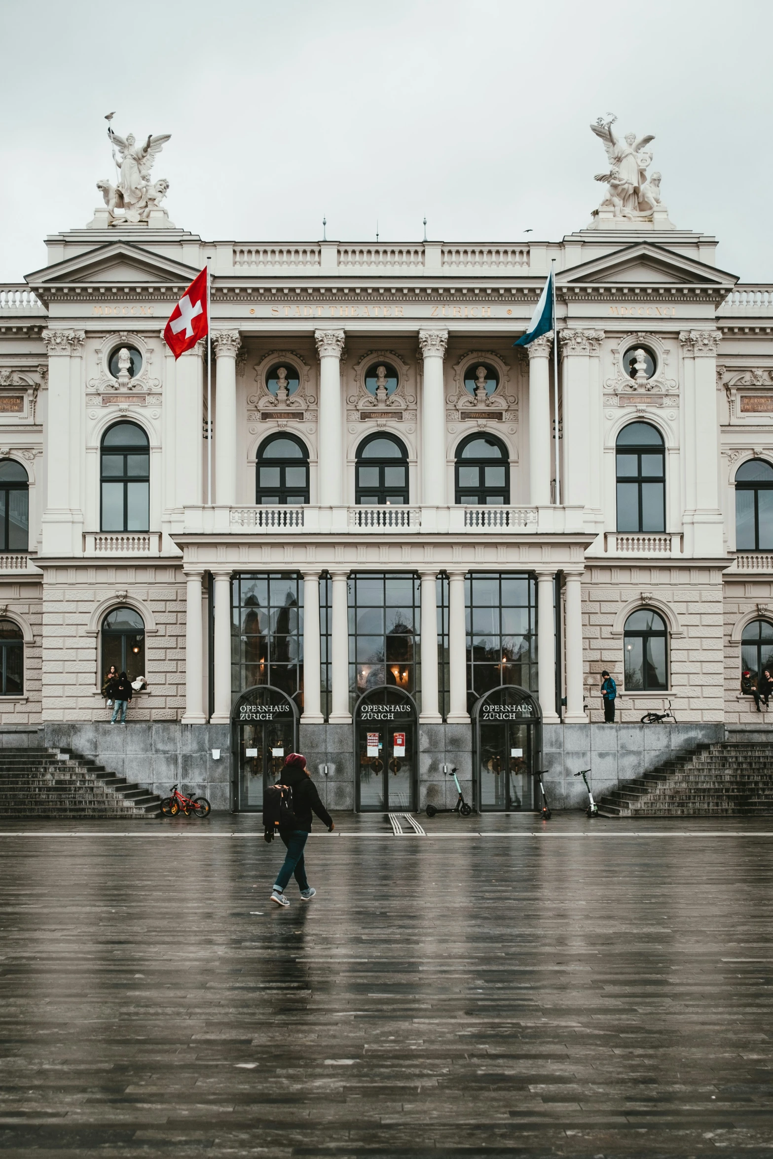 a couple of people walking across a wet floor in front of a large building