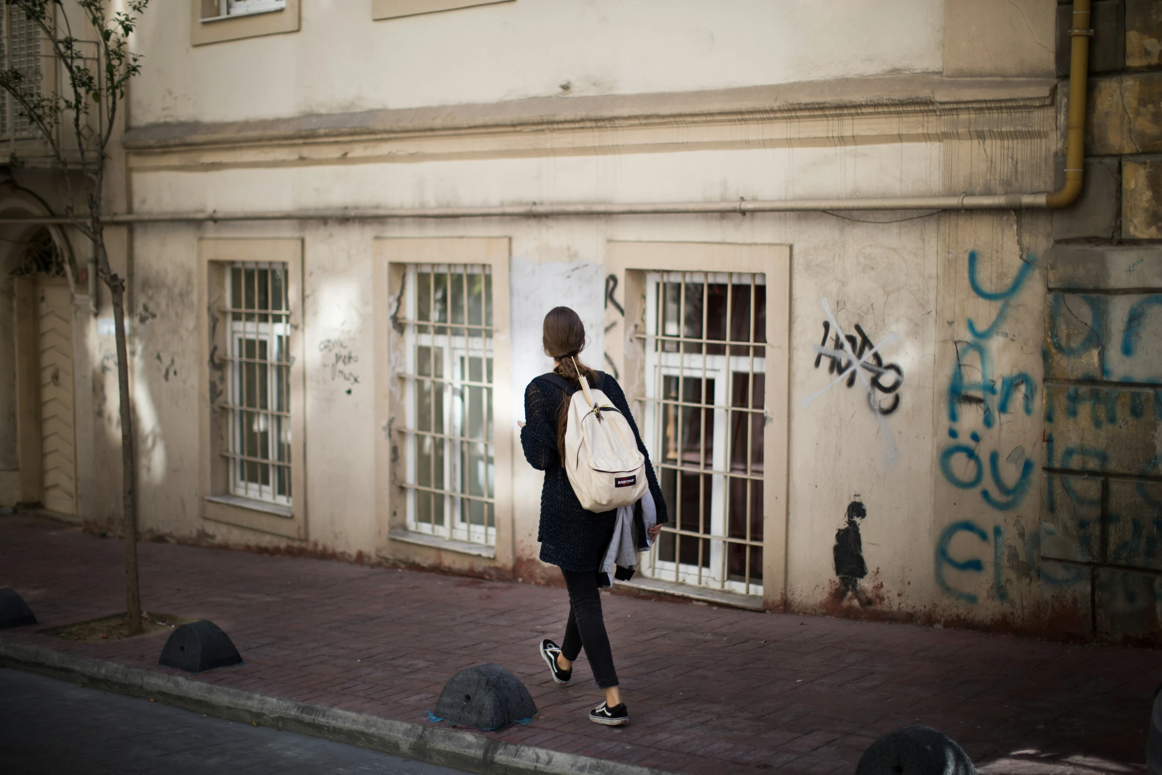 a woman with a white backpack walking past an old building