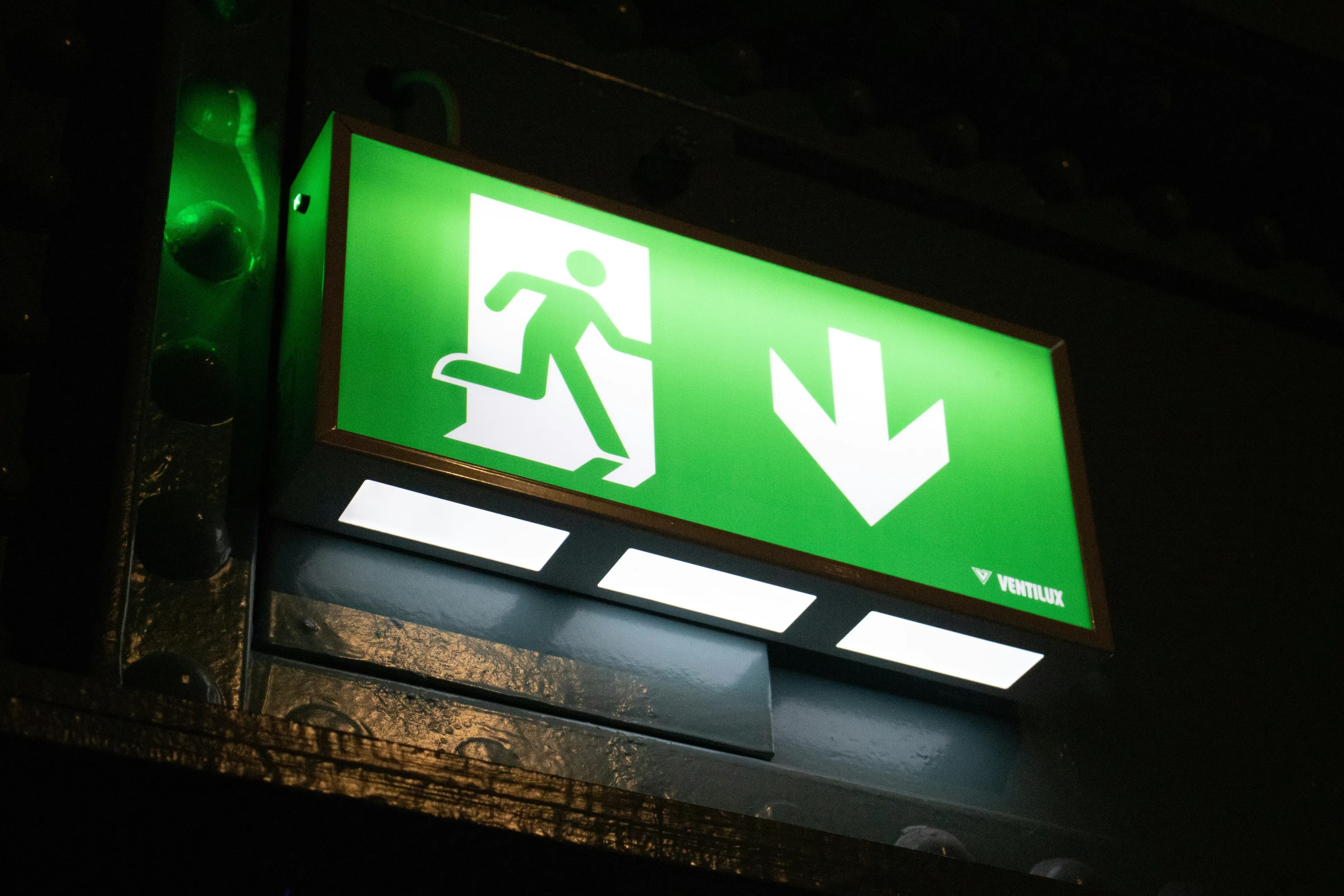 a green and white exit sign on a dark room