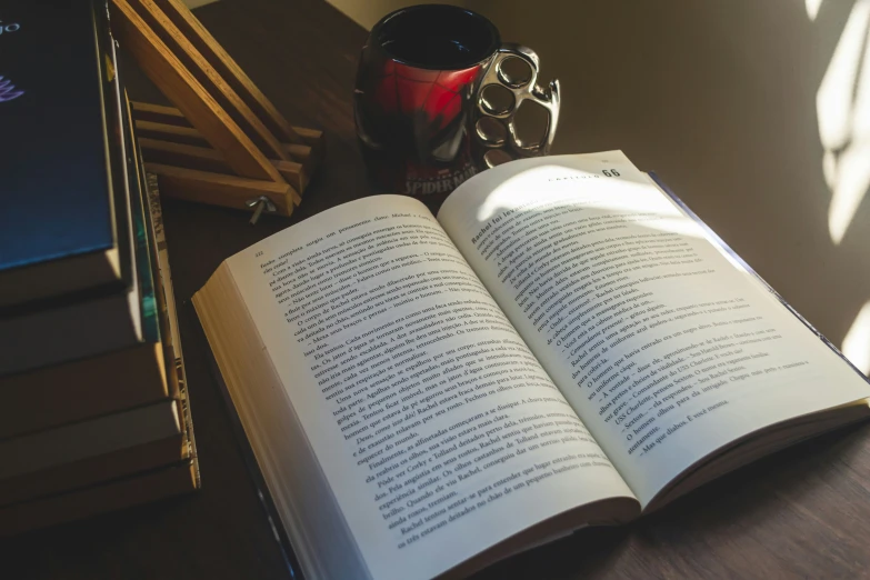 an open book next to a computer keyboard and coffee cup