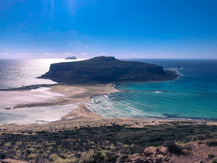 a sandy beach next to the ocean in front of mountains