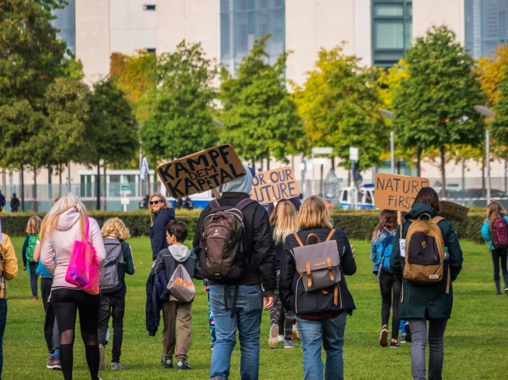 a group of people walking in the park with backpacks and signs