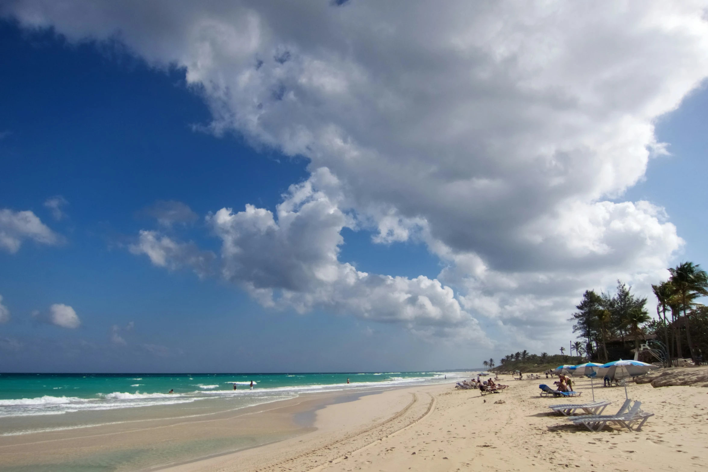 beach with two umbrellas and several people sitting under the sky