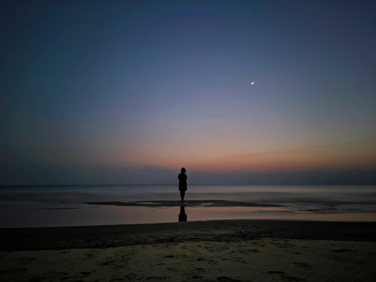 a man is standing at the water's edge during the sunset