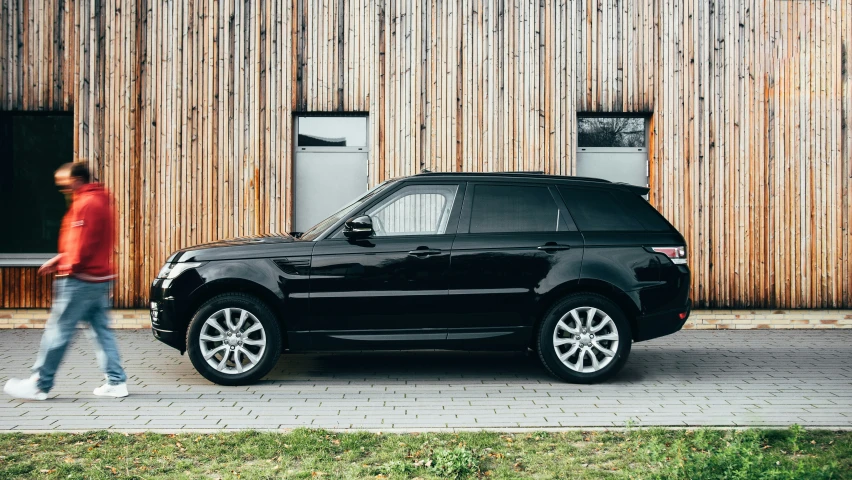 a man walking past a range rover in front of a wooden building