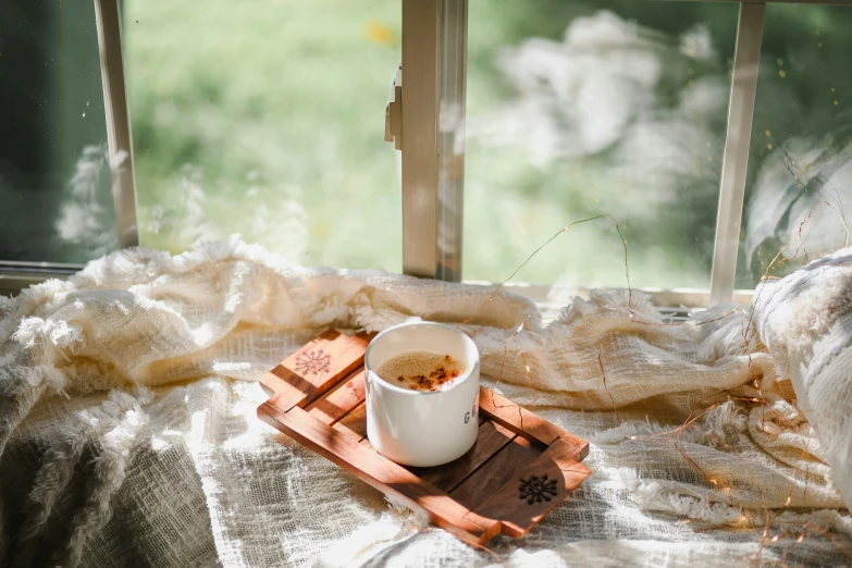 a cup of coffee sitting on a wooden tray in front of a window