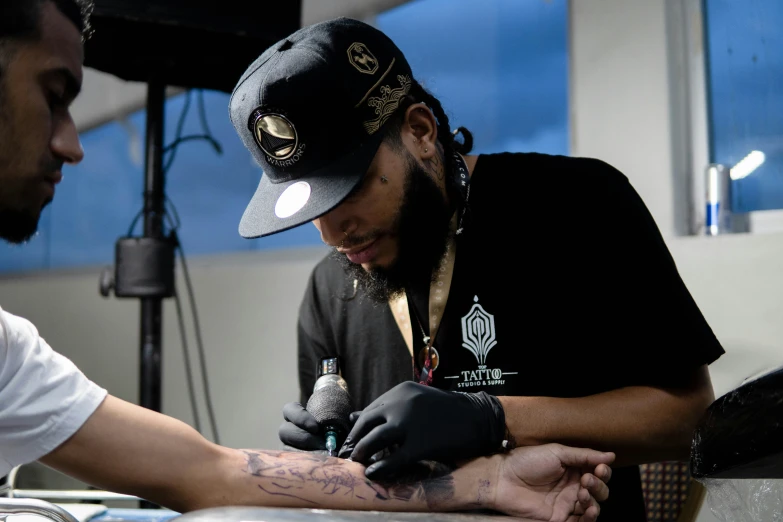 the man is working on his tattoo while another watches