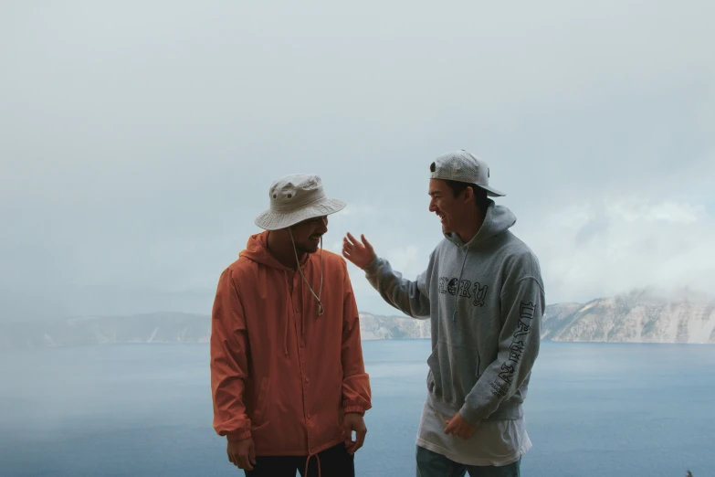 two men are standing by a lake in front of mountains