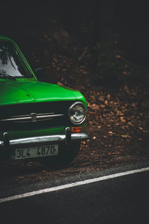 an old green car parked in the dirt