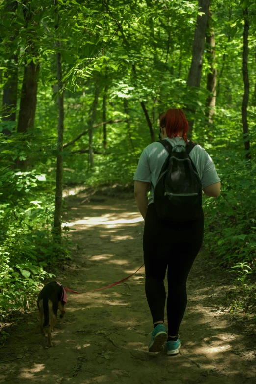 a woman with her red hair walking her dog in the woods