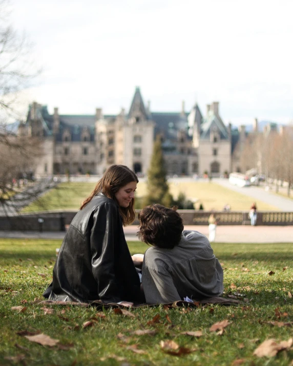 two young children sit on the grass and interact