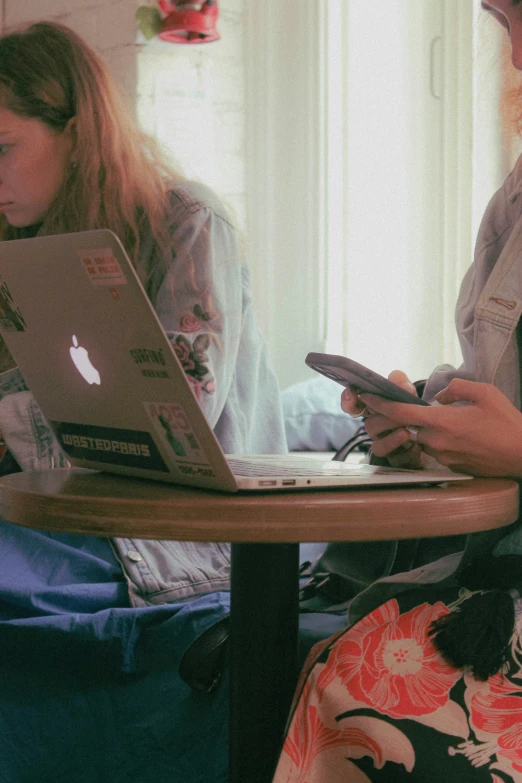 two girls using their cell phones while sitting at the table