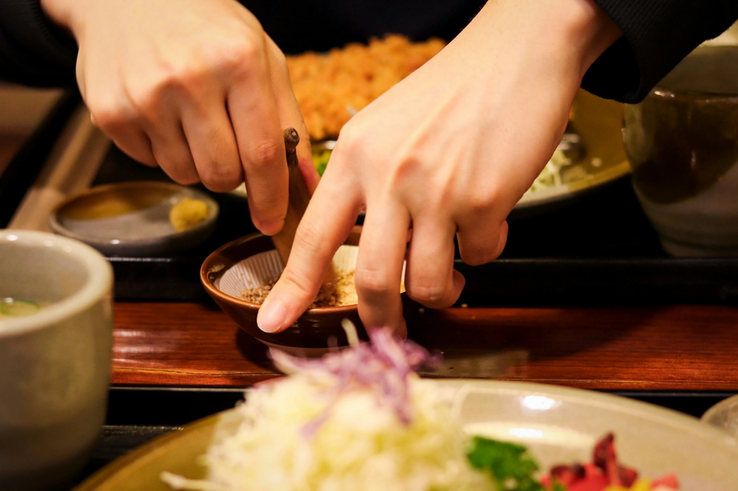 a woman in a blue jacket puts ingredients into a wooden bowl