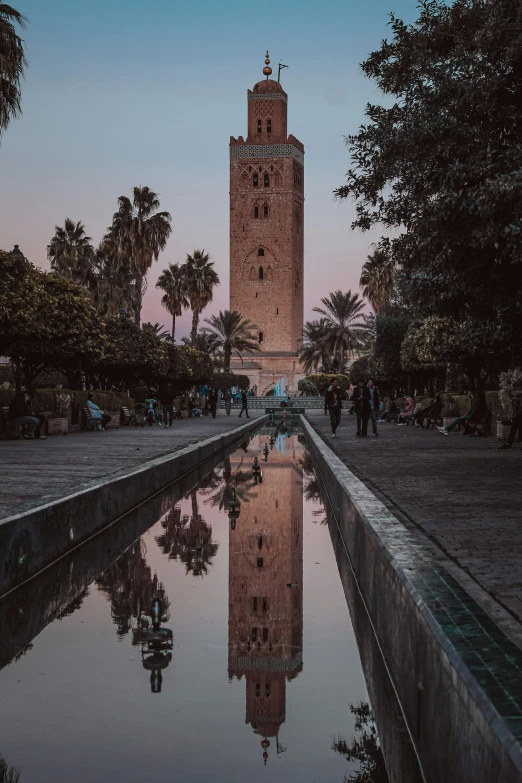 people and trees at dusk around a reflecting clock tower