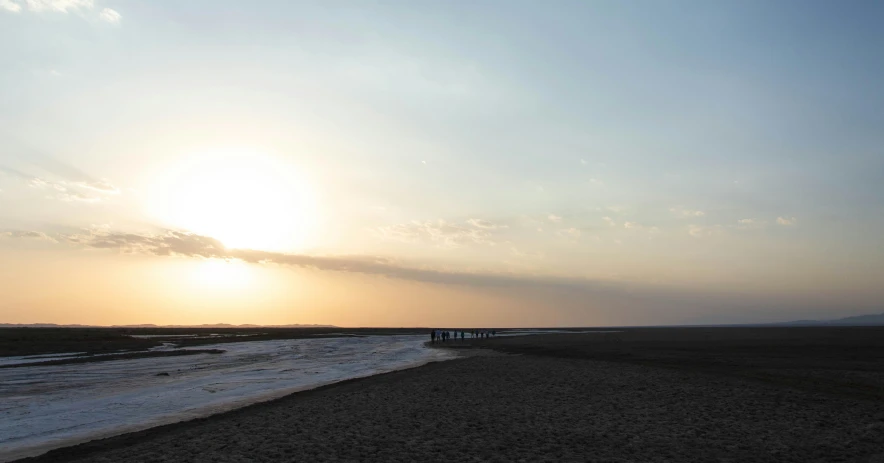 two people stand on a beach as the sun sets