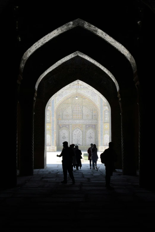 silhouettes of people standing underneath a bridge with light streaming through the arch